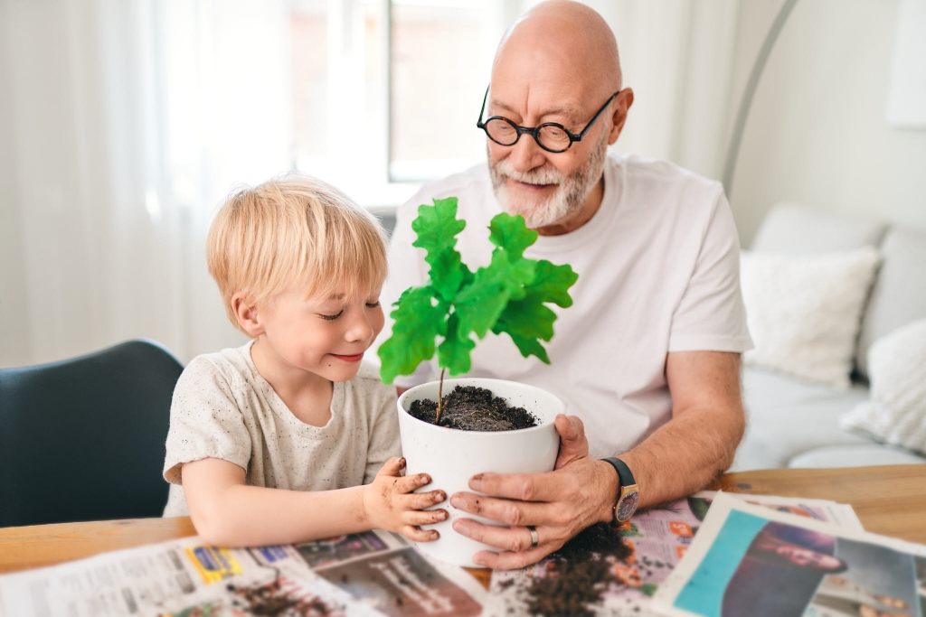 Isoisä ja lapsi istuttavat taimea ruukkuun.