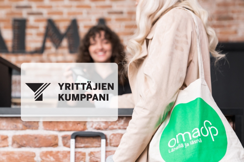 Nainen pankin kangaskassi olalla maksamassa hotellin vastaanotossa.