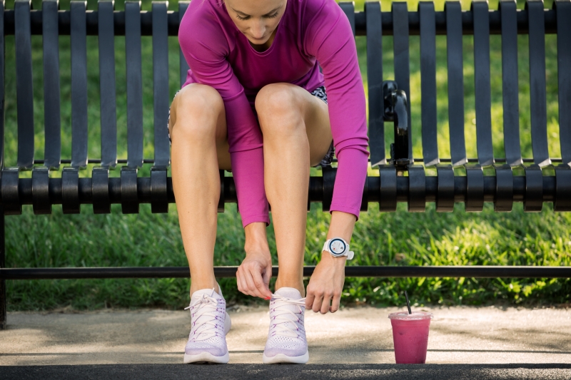 Lenkkeilijä sitoo kengännauhoja Garmin kello ranteessaan.