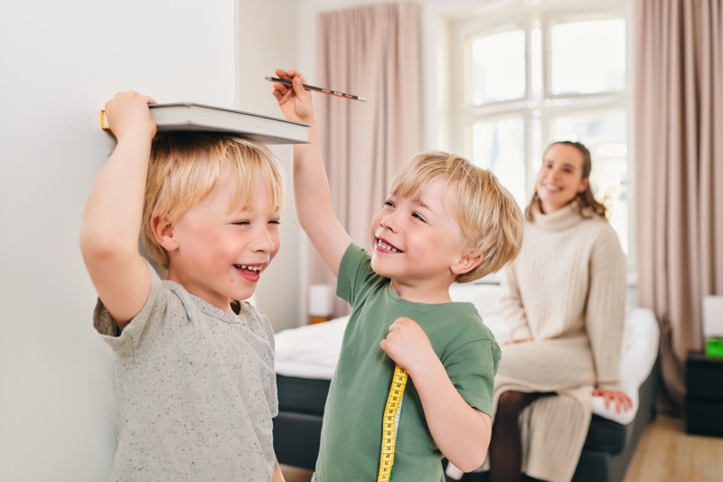 Lapset merkitsevät pituuksiaan seinälle äidin katsellessa.