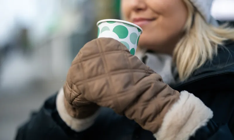 Henkilö juo kahvikupista ulkona ja hymyilee.