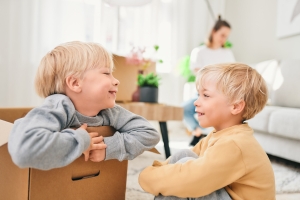 Lapset leikkivät muuttolaatikoissa aikuisen pakatessa.