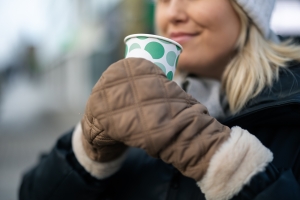 Henkilö juo kahvikupista ulkona ja hymyilee.