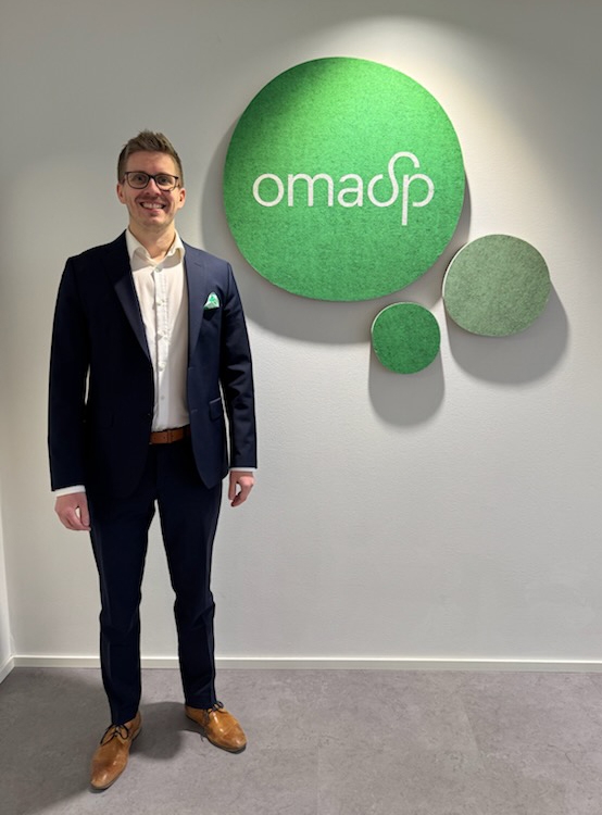 Seisomassa Olli Ilmarinen, taustalla vihreä palloelementti, jossa OmaSp:n logo